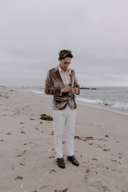A man in a velvet suit stands on a cloudy beach, symbolizing fashion and contemplation.