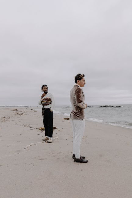 Stylish men in suits pose on a sandy beach under an overcast sky, creating a fashion-forward scene.