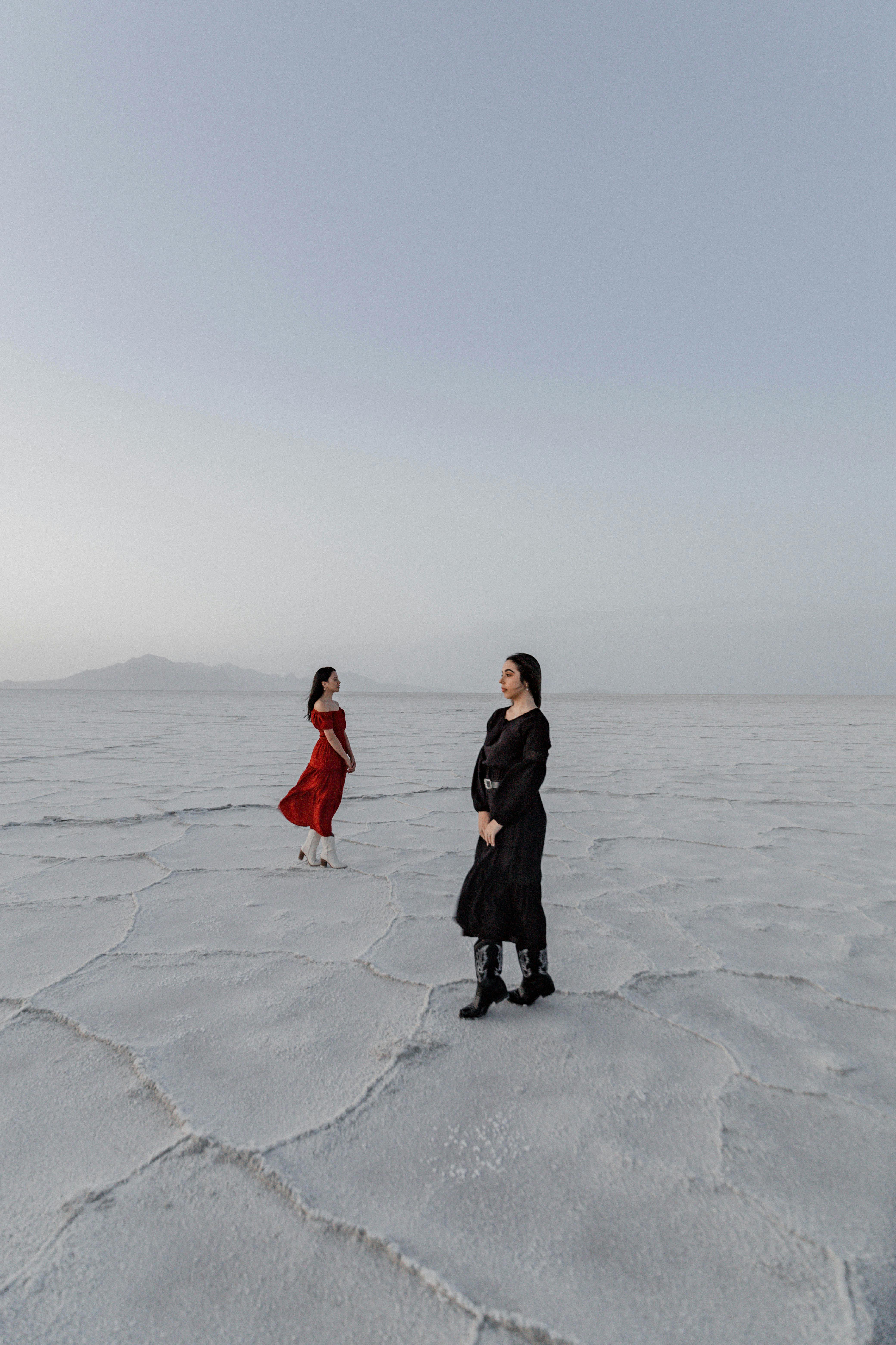 Two women in elegant dresses posing on a vast salt flat under a clear sky.