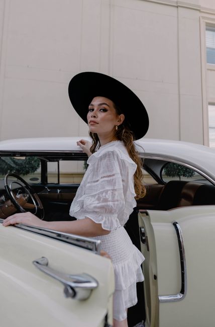 Stylish woman in vintage attire posing gracefully with a classic car. Perfect for retro-themed presentations.