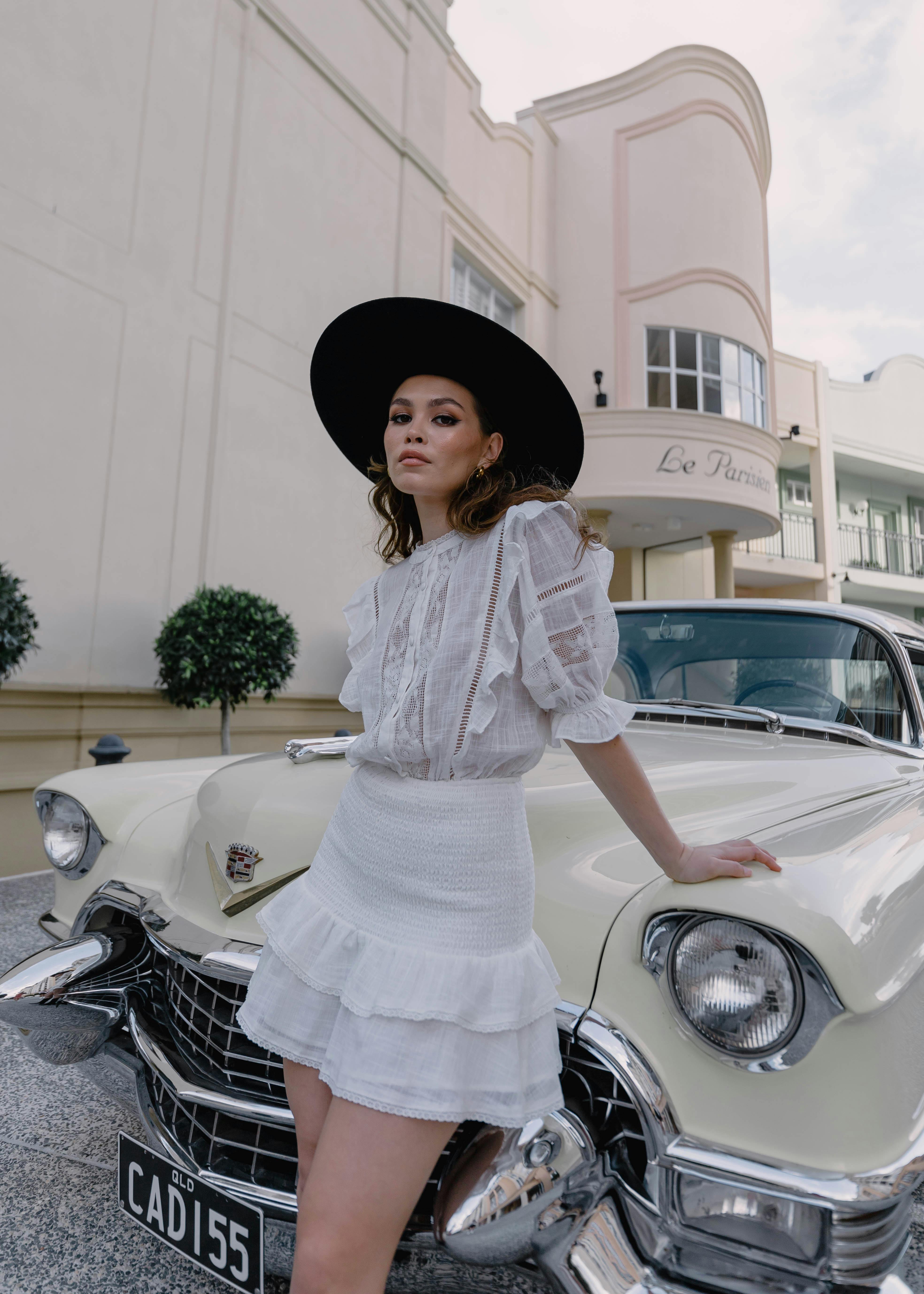 woman in hat and skirt posing by vintage car