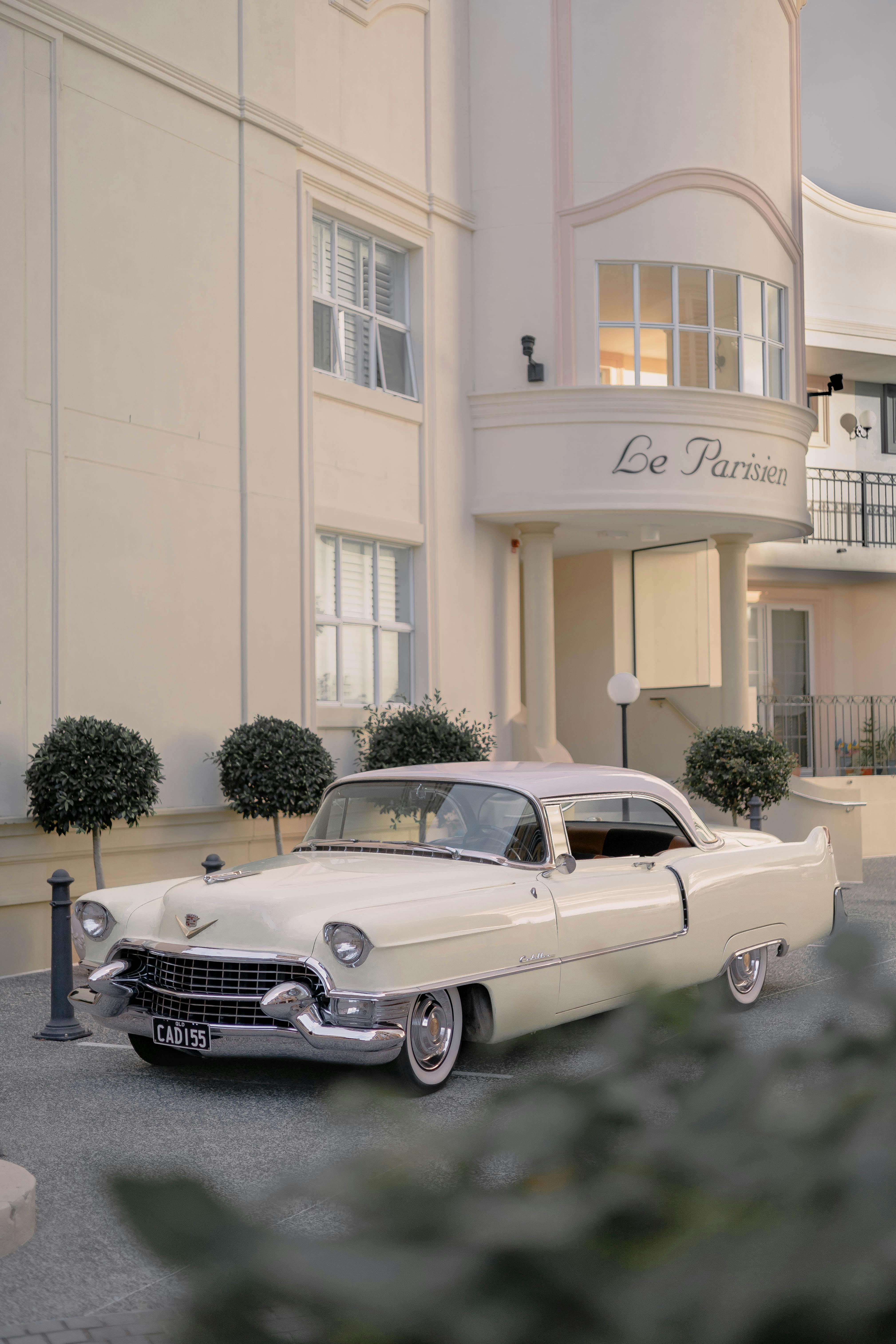 A classic white car parked outside the luxury hotel Le Parisien, capturing vintage elegance.