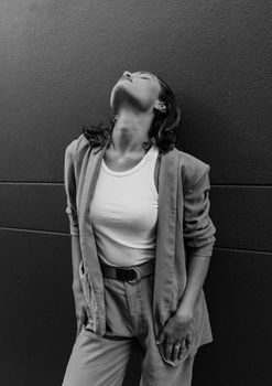 Striking black and white portrait of a woman posing against a wall, emitting a sense of elegance and confidence.