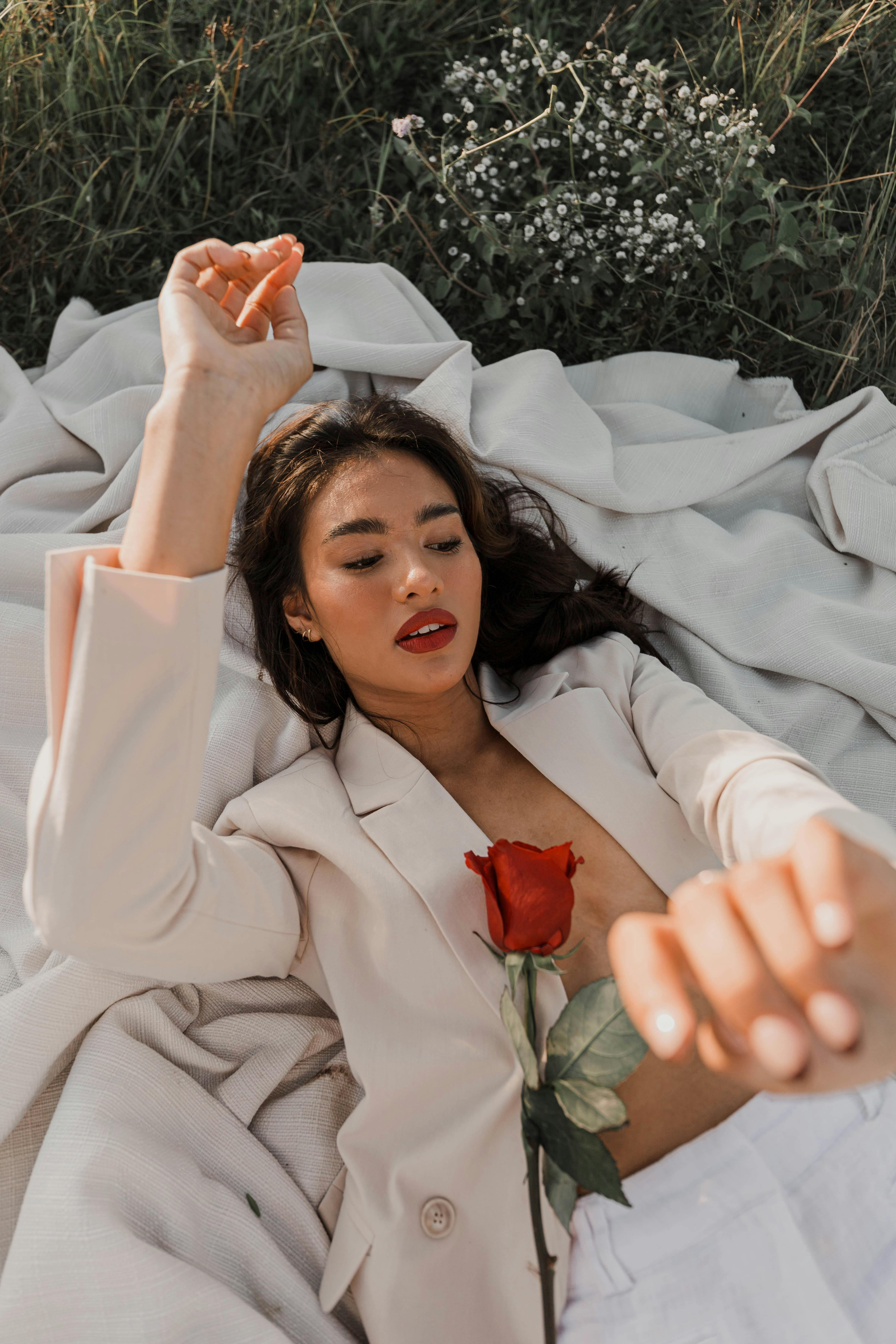Stylish woman lying with a rose on white fabric surrounded by nature.