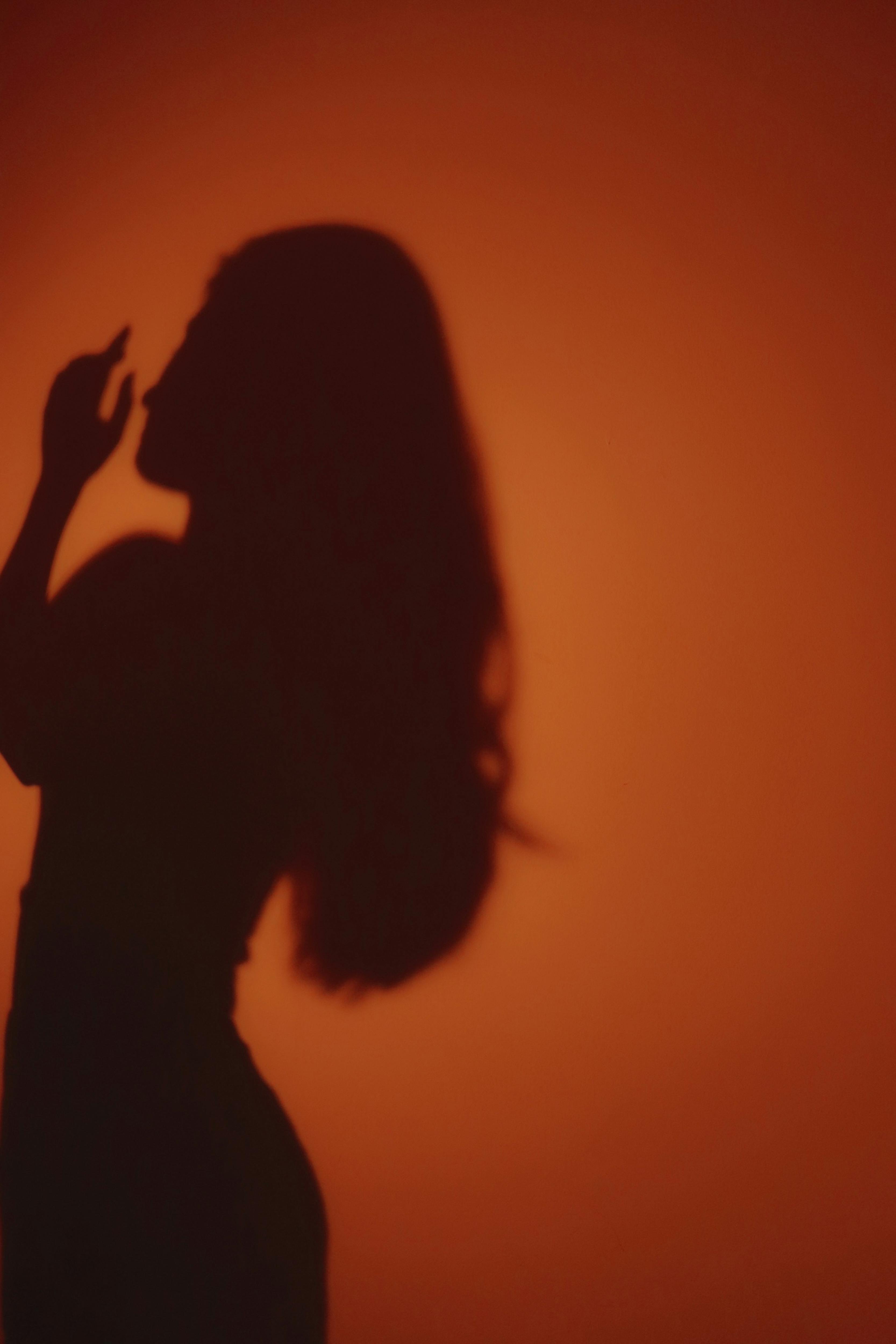 A dramatic silhouette of a woman with long hair against a warm orange background.