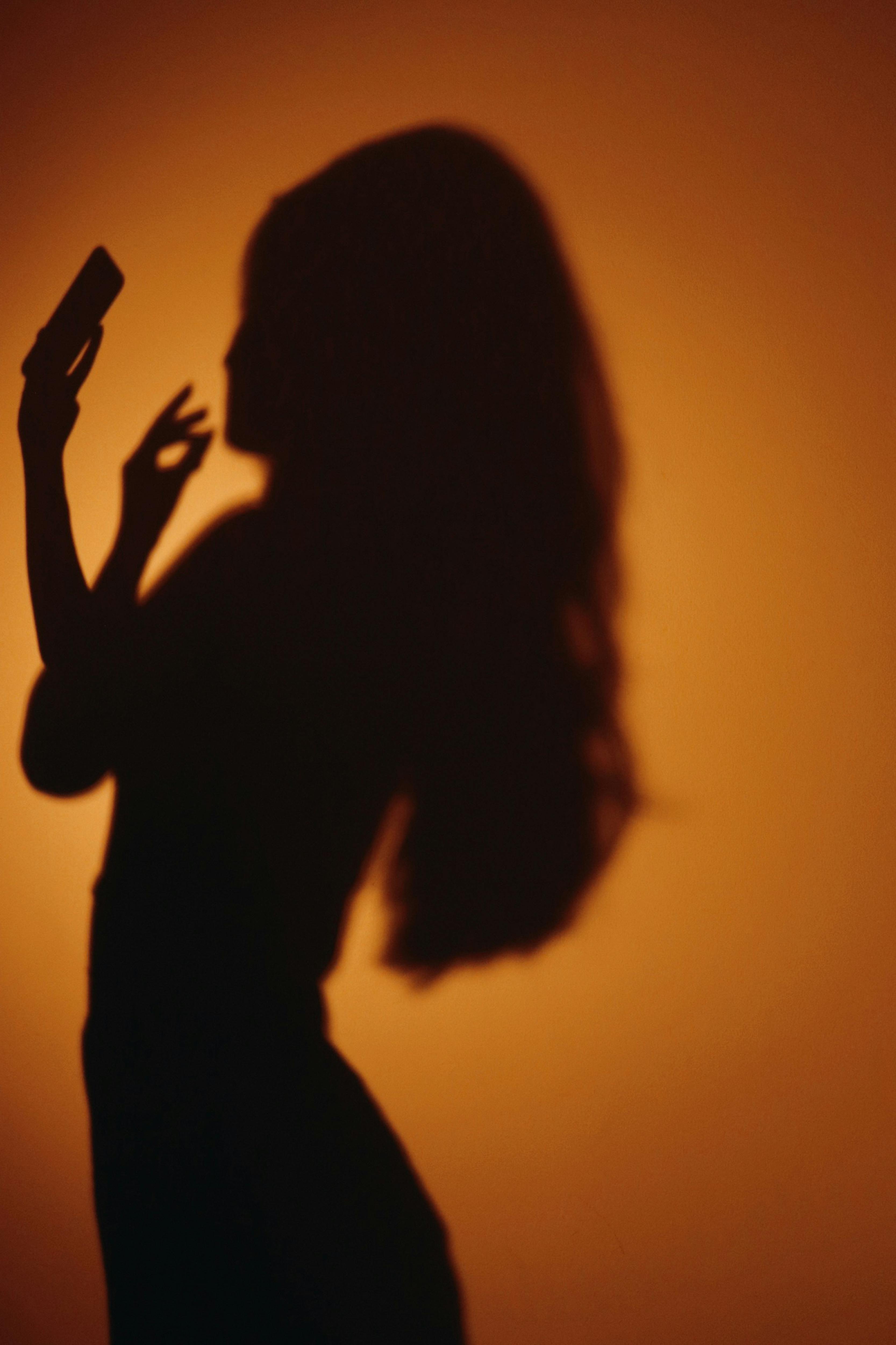 Silhouette of a woman holding a smartphone against a sunset background in Paris.