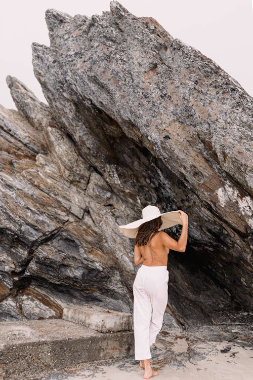 Woman in Hat Posing Topless near Rocks