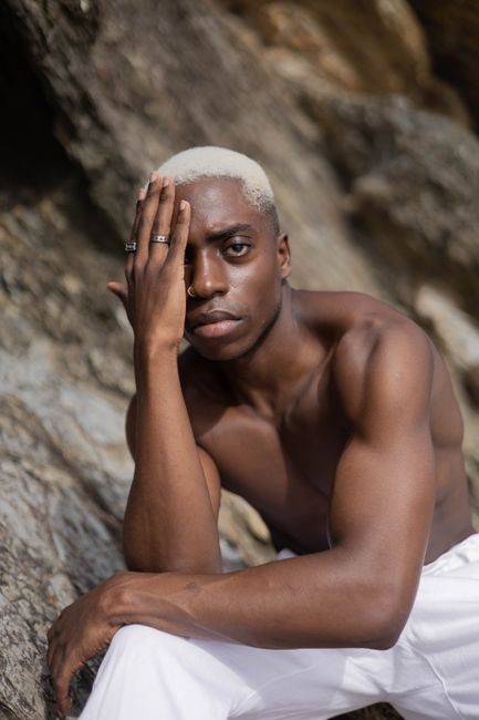 Portrait of a young man with platinum dyed hair sitting outdoors against a rock background.