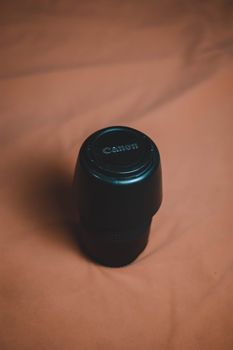 A Canon camera lens rests on a soft fabric surface, captured in a vertical shot.