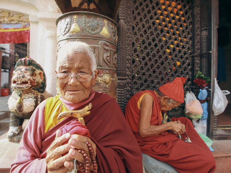 Old Monk In Traditional Clothes Sitting Near Temple