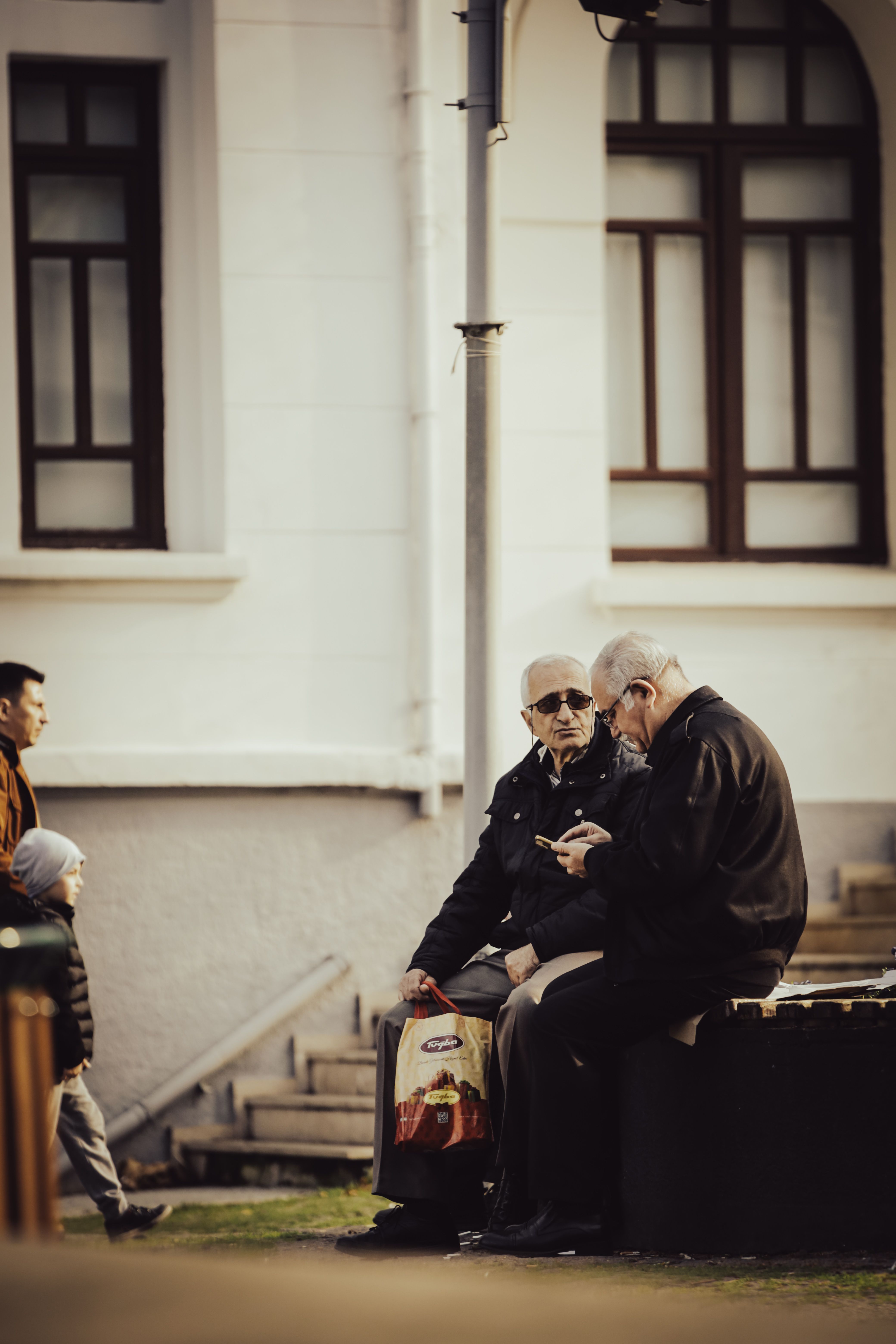 Senior men chatting on a bench in Bursa, Turkey, near a building facade.