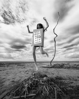 Artistic black and white photo of woman jumping on beach with a box.