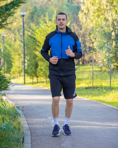 Free Man jogging on a tree-lined path in a sunny park wearing sportswear. Stock Photo