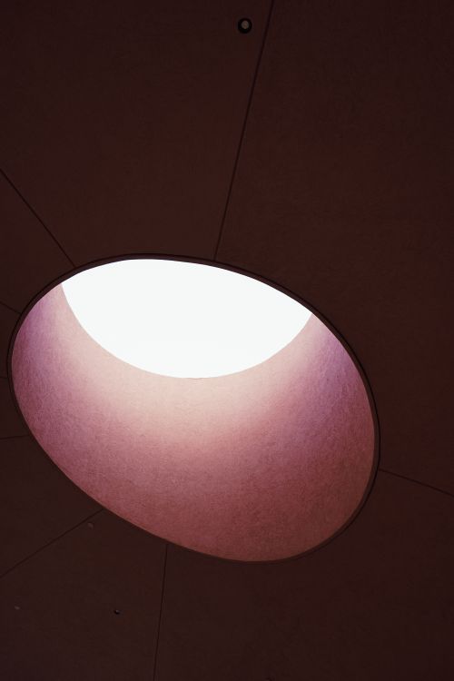 Free A round skylight casts a dramatic light on dark walls, creating an abstract and moody ambiance. Stock Photo