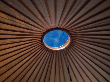 View from inside a structure with a central skylight revealing a clear blue sky through wooden beams.