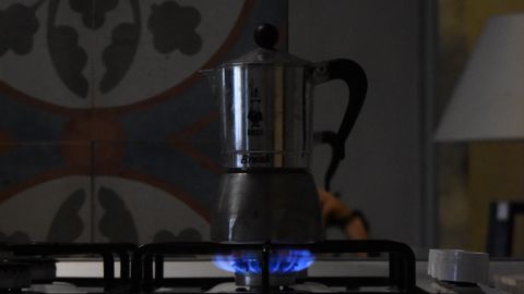 A Moka pot brewing coffee on a lit gas stove in a cozy kitchen setting.