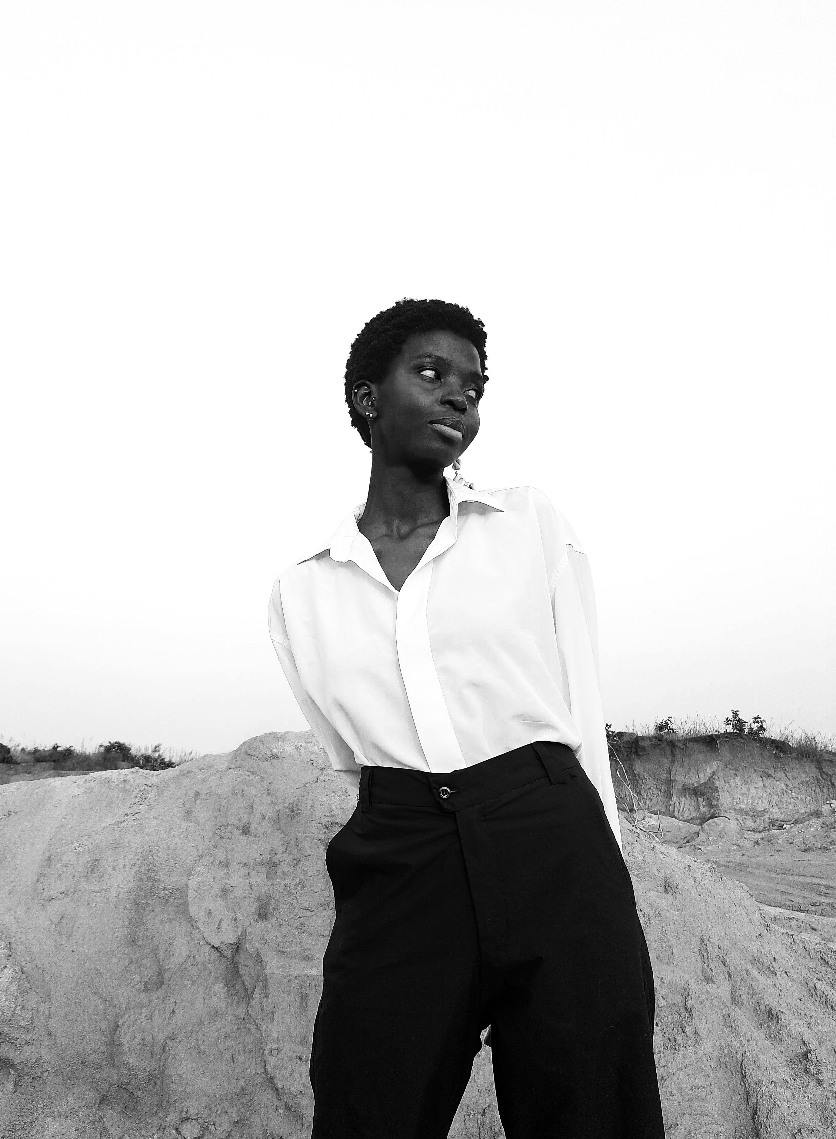 Elegant monochrome portrait of an African woman wearing a white shirt and black pants, standing outdoors.