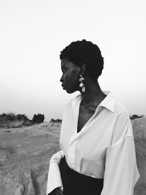 Black and white portrait of a woman with statement earrings in a desert setting.