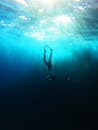 一个自由潜水者在深蓝色的海洋中水下游泳的剪影，被阳光的光线包围