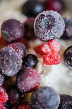 Detailed macro shot of frozen mixed berries on creamy yogurt, showcasing textures and vibrant colors.