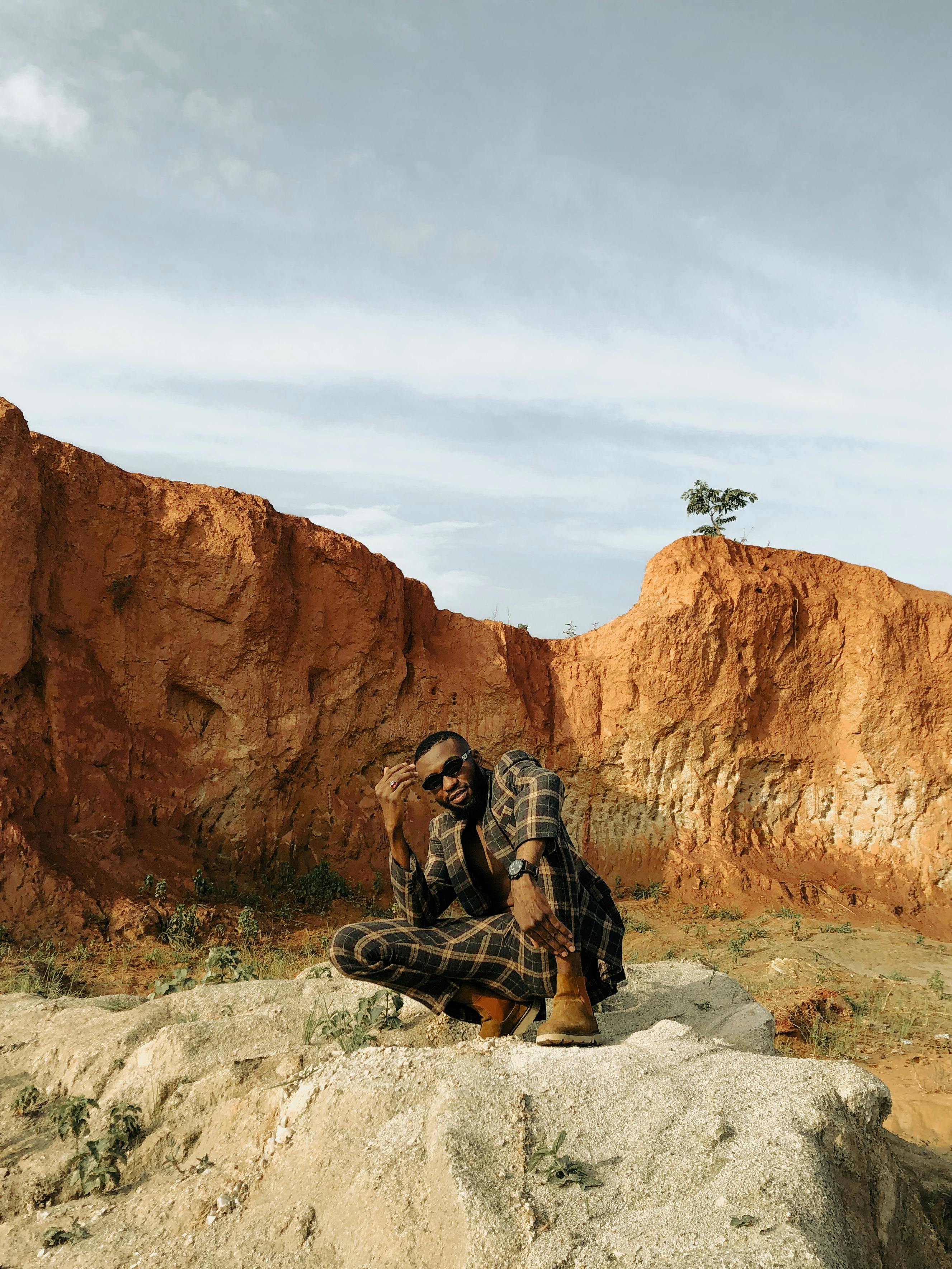 A fashion model poses in an arid landscape with rocky formations under a clear sky, exuding style and confidence.