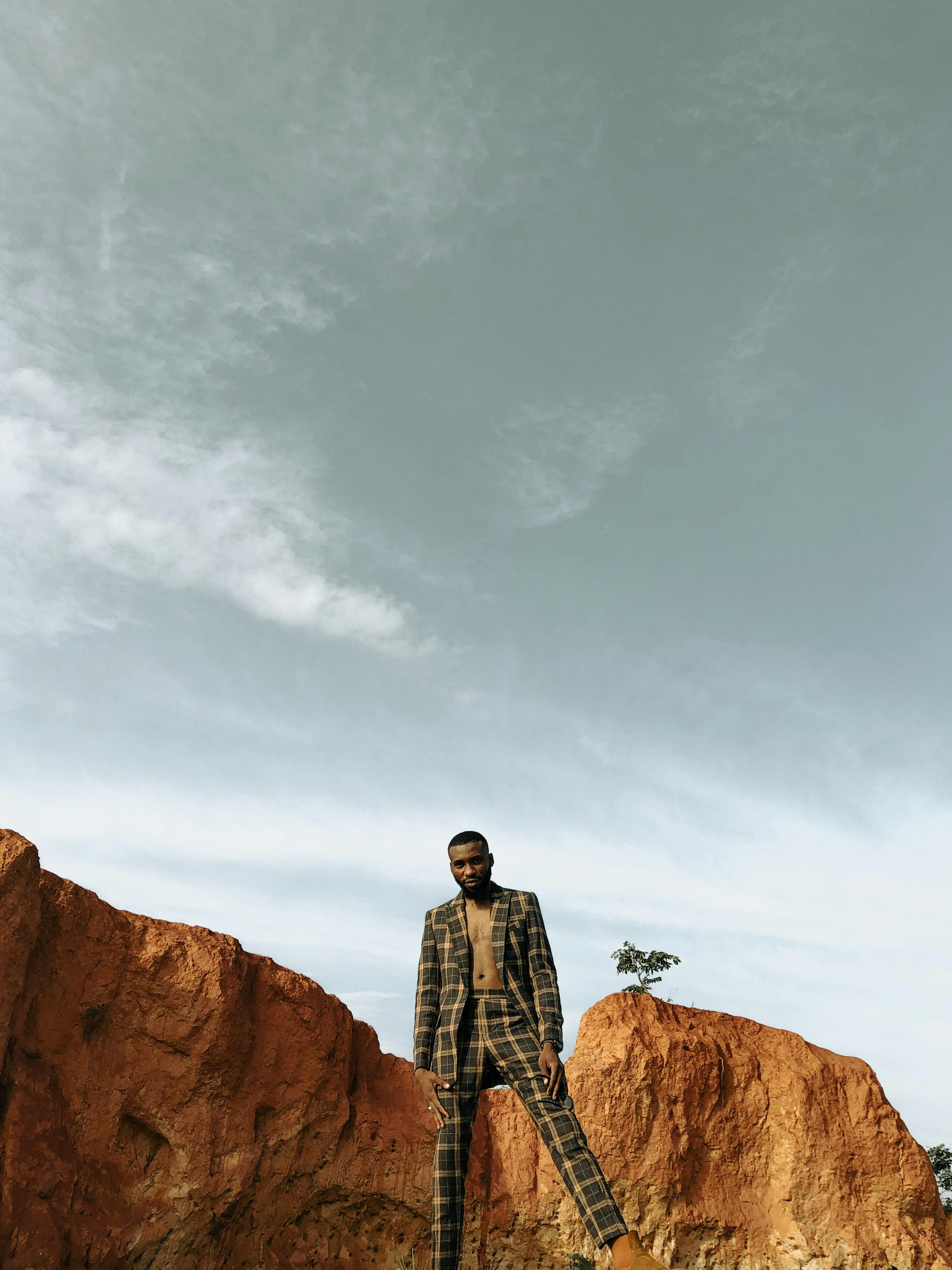 Stylish man in a suit against rocky terrain under a clear sky, showcasing fashion in nature.