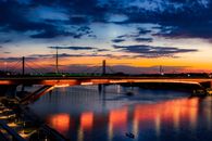 Scenic view of a bridge in Belgrade at twilight with colorful reflections and a crescent moon.