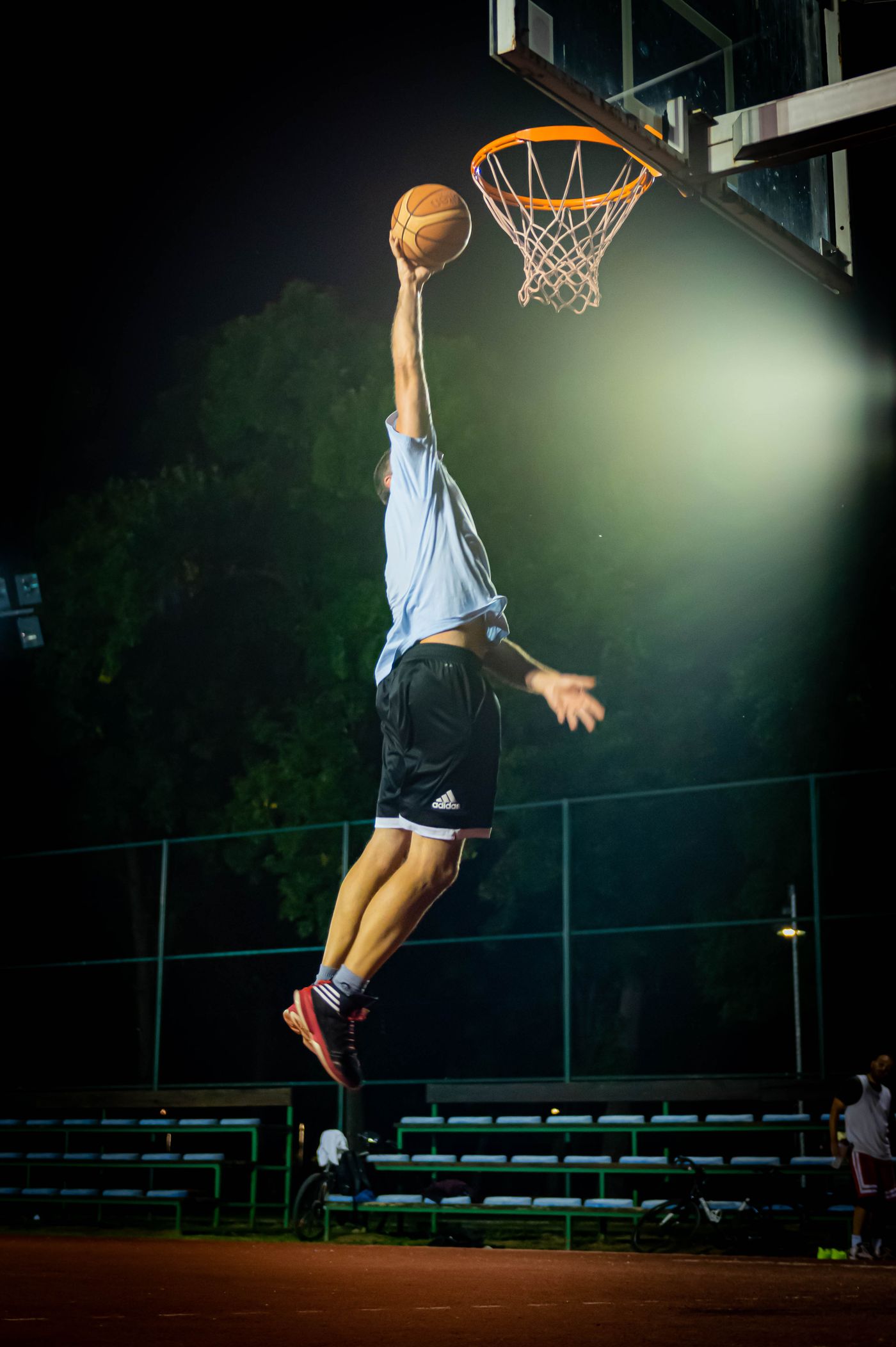 Basketball player performing a slam dunk under bright lights on an outdoor court at night
