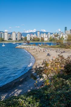 A scenic view of Vancouver's skyline with a busy beachfront under clear blue skies in autumn.