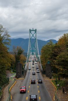Cars crossing the iconic Lions Gate Bridge in Vancouver, surrounded by autumn foliage and mountains.