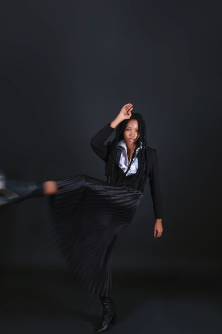 A black woman in a stylish jacket performing a high kick in a studio setting.