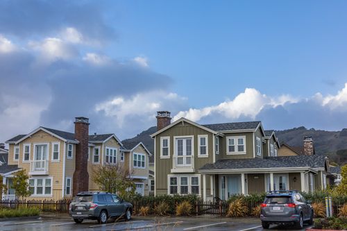 Free Picturesque suburban neighborhood with modern houses and parked cars under a partly cloudy sky. Stock Photo