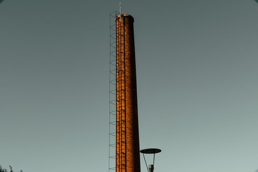 Tall industrial chimney with ladder against a clear sky backdrop, no pollution visible.