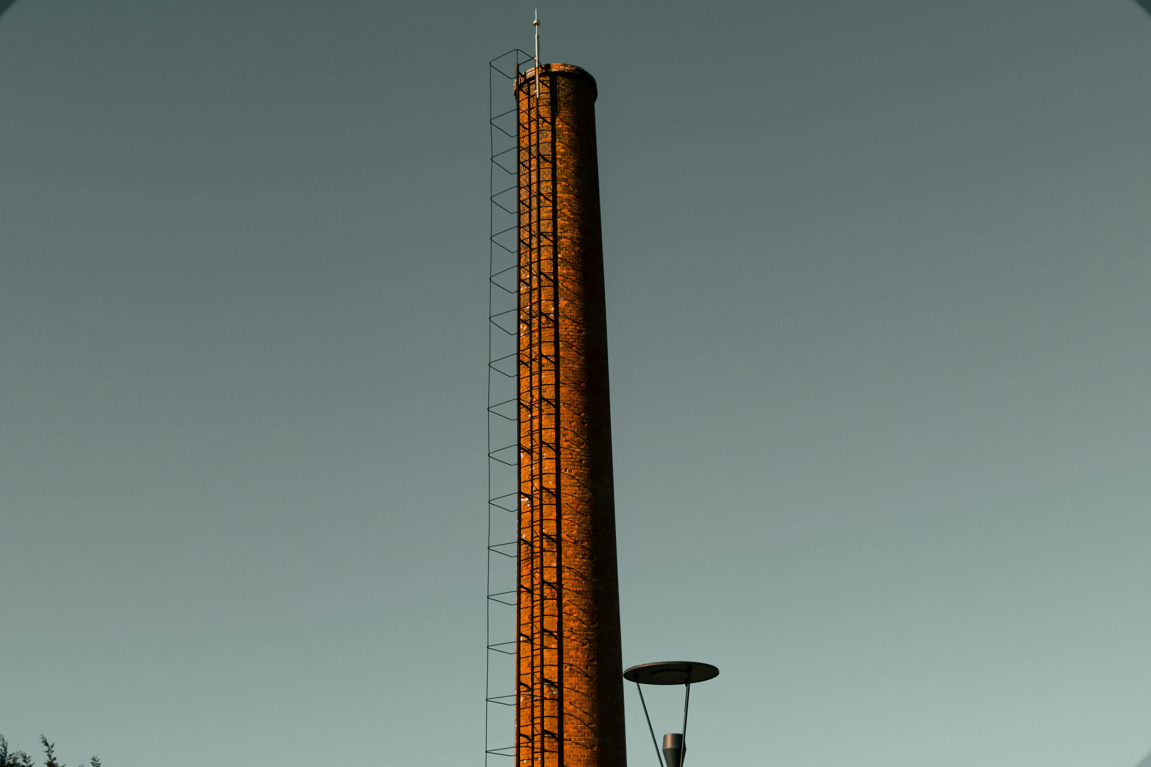 Free Tall industrial chimney with ladder against a clear sky backdrop, no pollution visible. Stock Photo