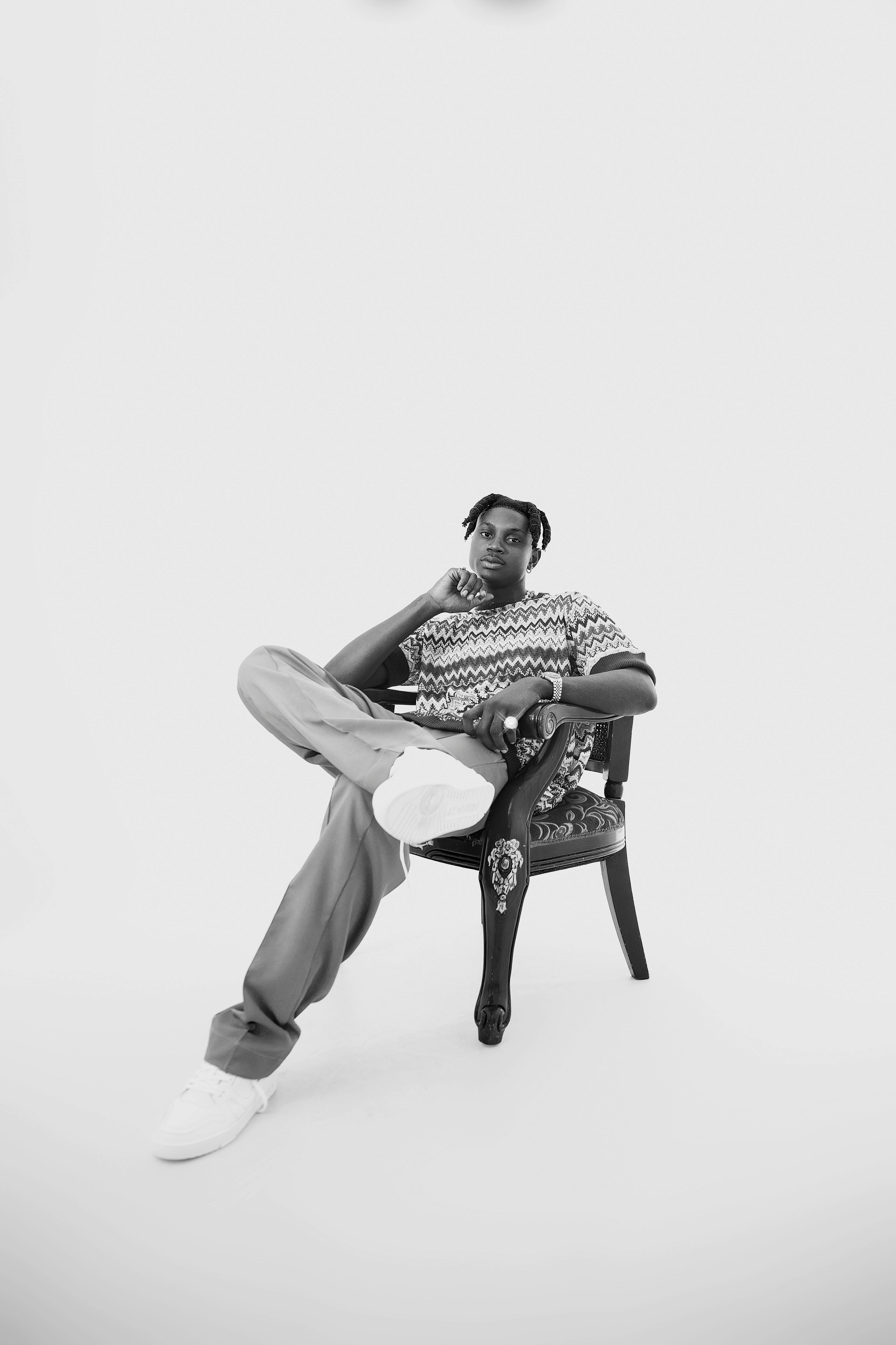 Black and white portrait of a stylish African American man sitting in a chair in a studio setting.