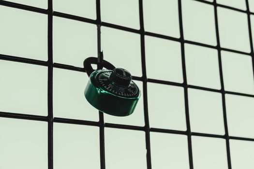 A green combination lock is attached to a wire fence grid, symbolizing security.
