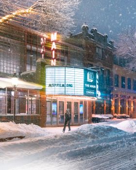 Snowy street view of The Main Cinema in Minneapolis, showcasing its illuminated facade during a winter evening.