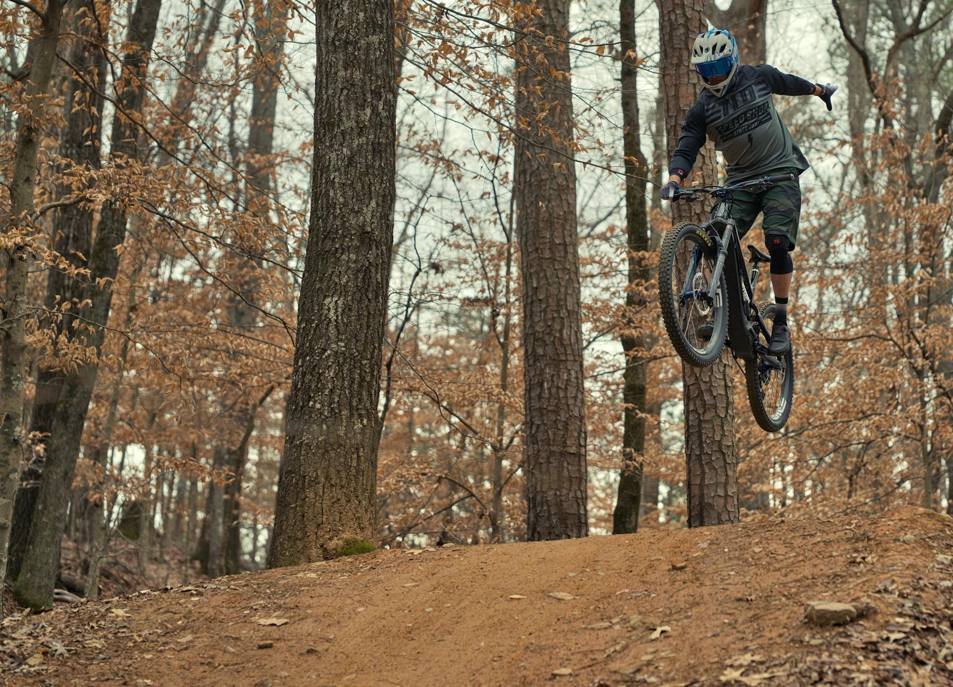 A mountain biker jumps in a forest during fall at Big Creek, GA, showcasing skill and adrenaline.