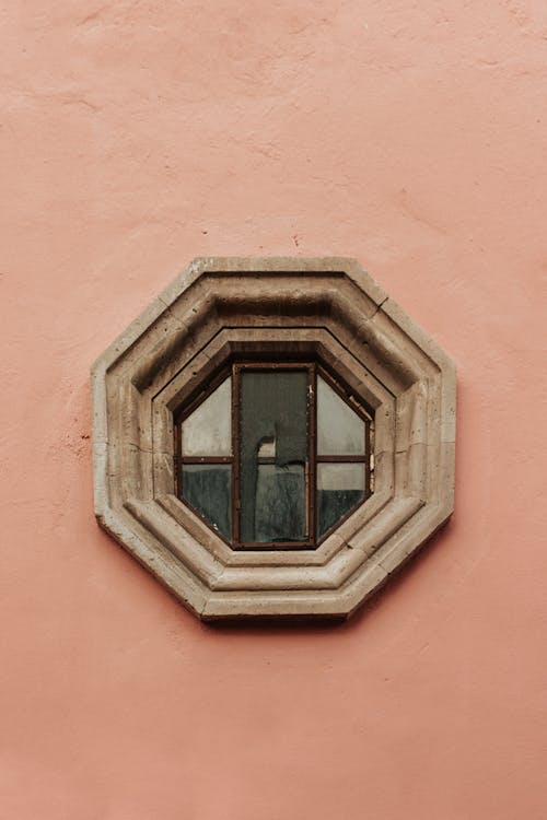 An Octagon Window with a Wooden Frame in a Pink Building 