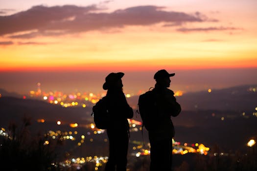 Two hikers silhouetted against a vibrant sunset over Taipei, creating a serene and adventurous scene.