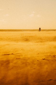A distant figure walks along a sandy beach in Los Angeles under warm lighting, evoking a tranquil atmosphere.