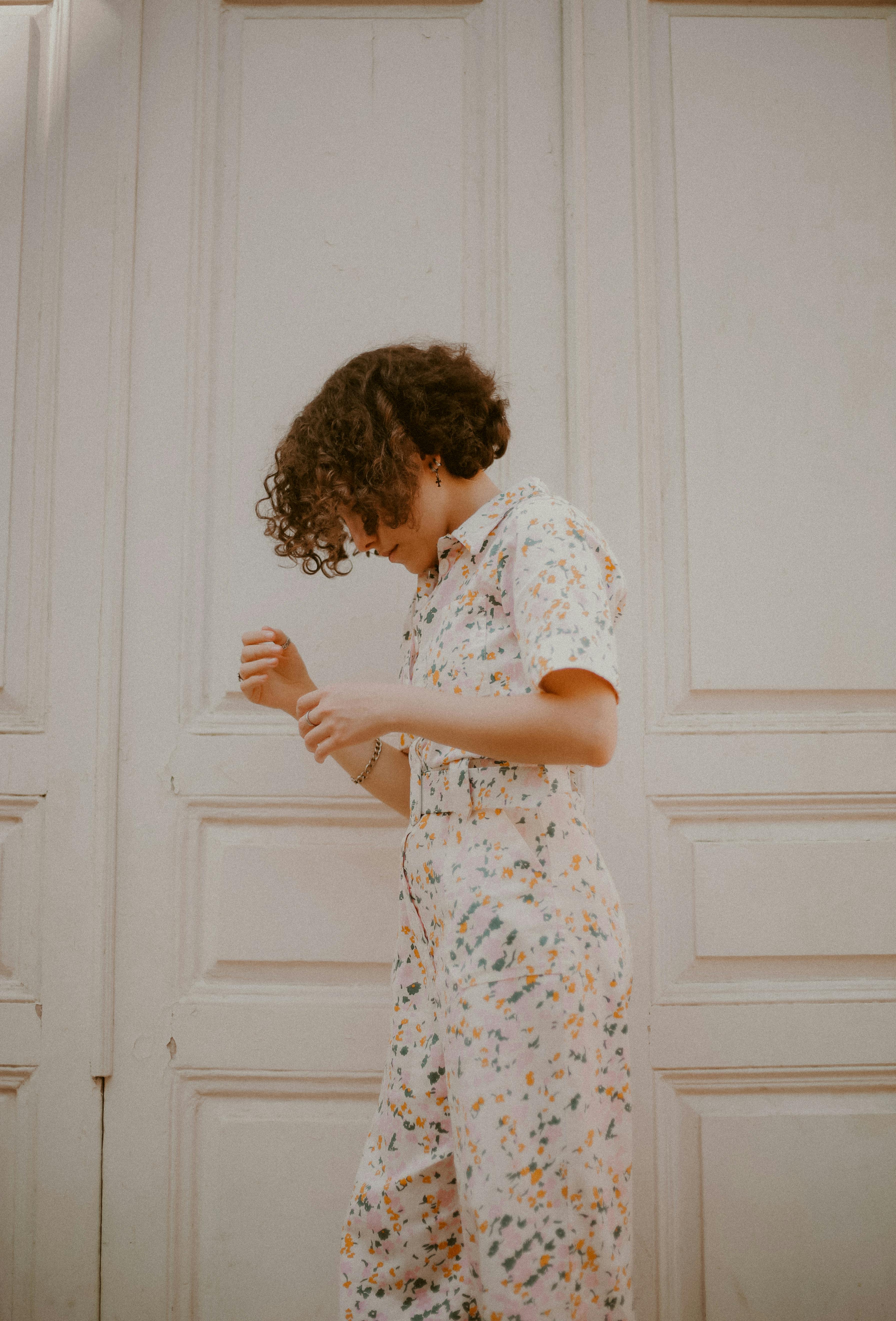Free A stylish woman with curly hair in a floral jumpsuit poses against a wooden white wall in Baku. Stock Photo