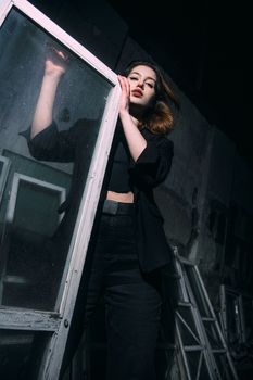 Stylish woman in dark fashion poses dramatically with a window frame, conveying elegance.