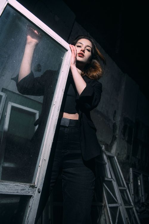 Free Stylish woman in dark fashion poses dramatically with a window frame, conveying elegance. Stock Photo
