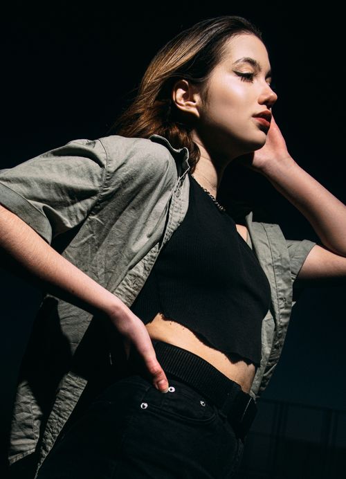 Free Stylish young woman in a black crop top posing with confidence in dramatic sunlight. Stock Photo