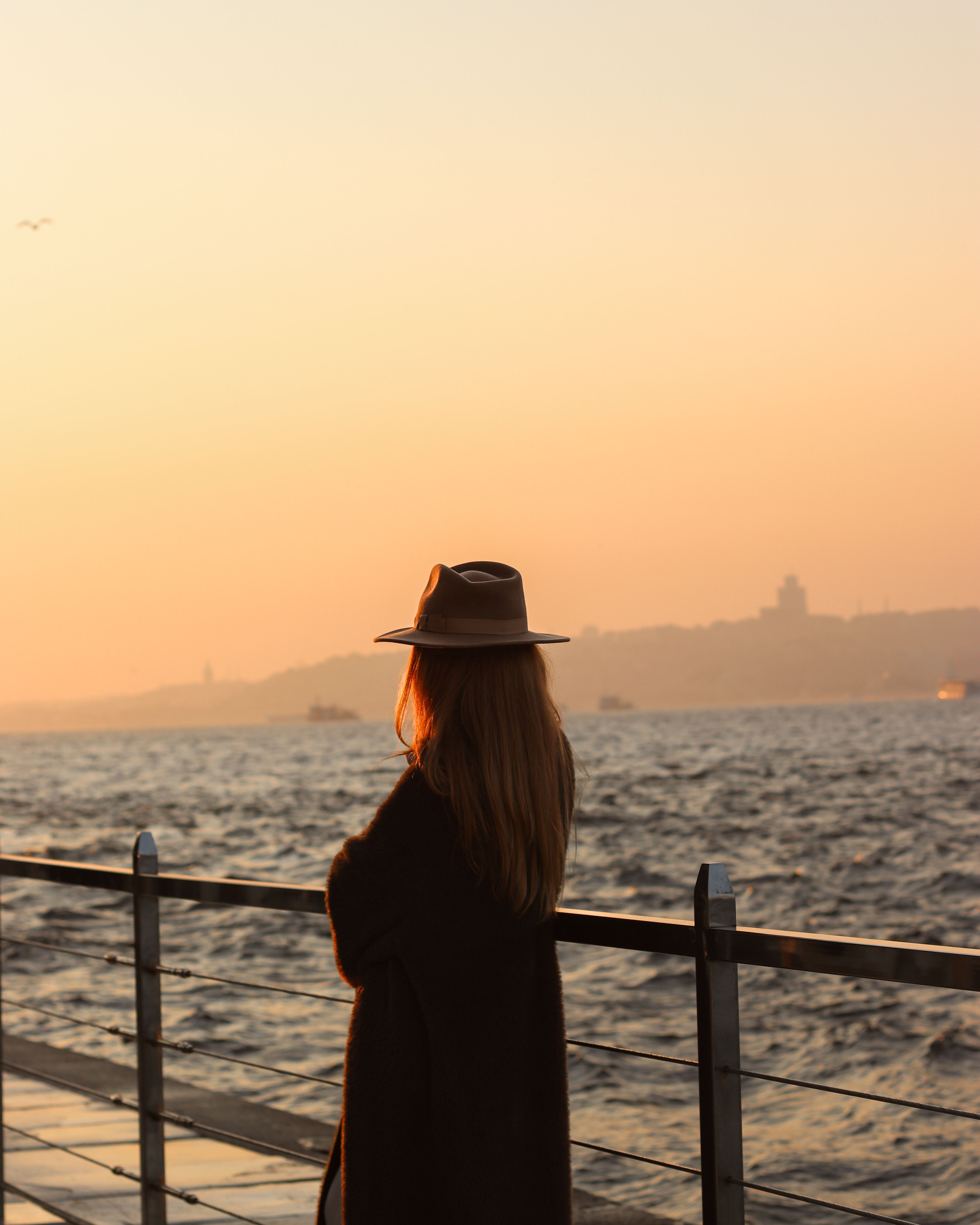 Woman in a Hat and Coat Looking at the View of Sea at Dusk · Free Stock ...