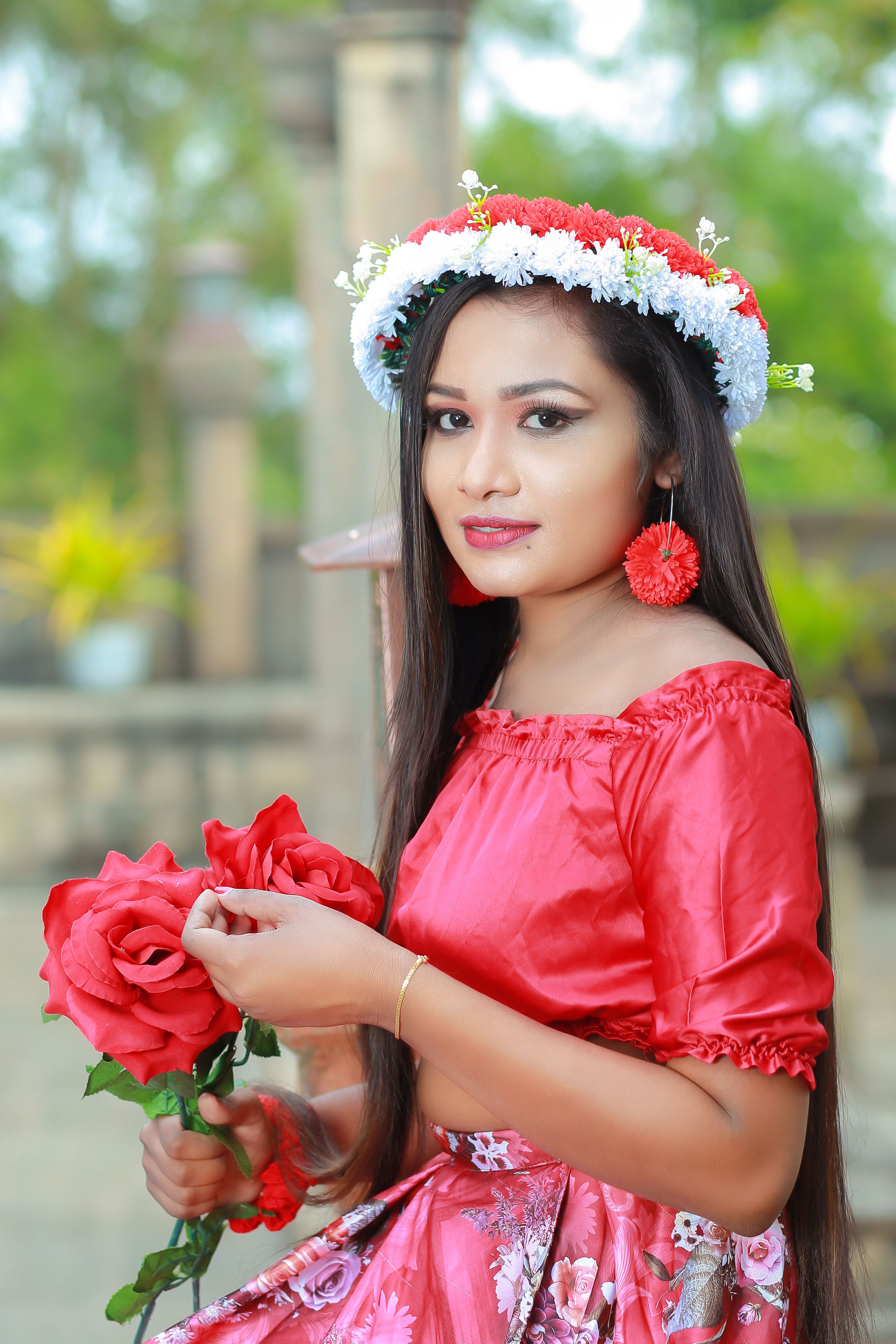 A woman in vibrant red attire with a floral wreath and roses outdoors. Perfect for fashion and seasonal concepts.