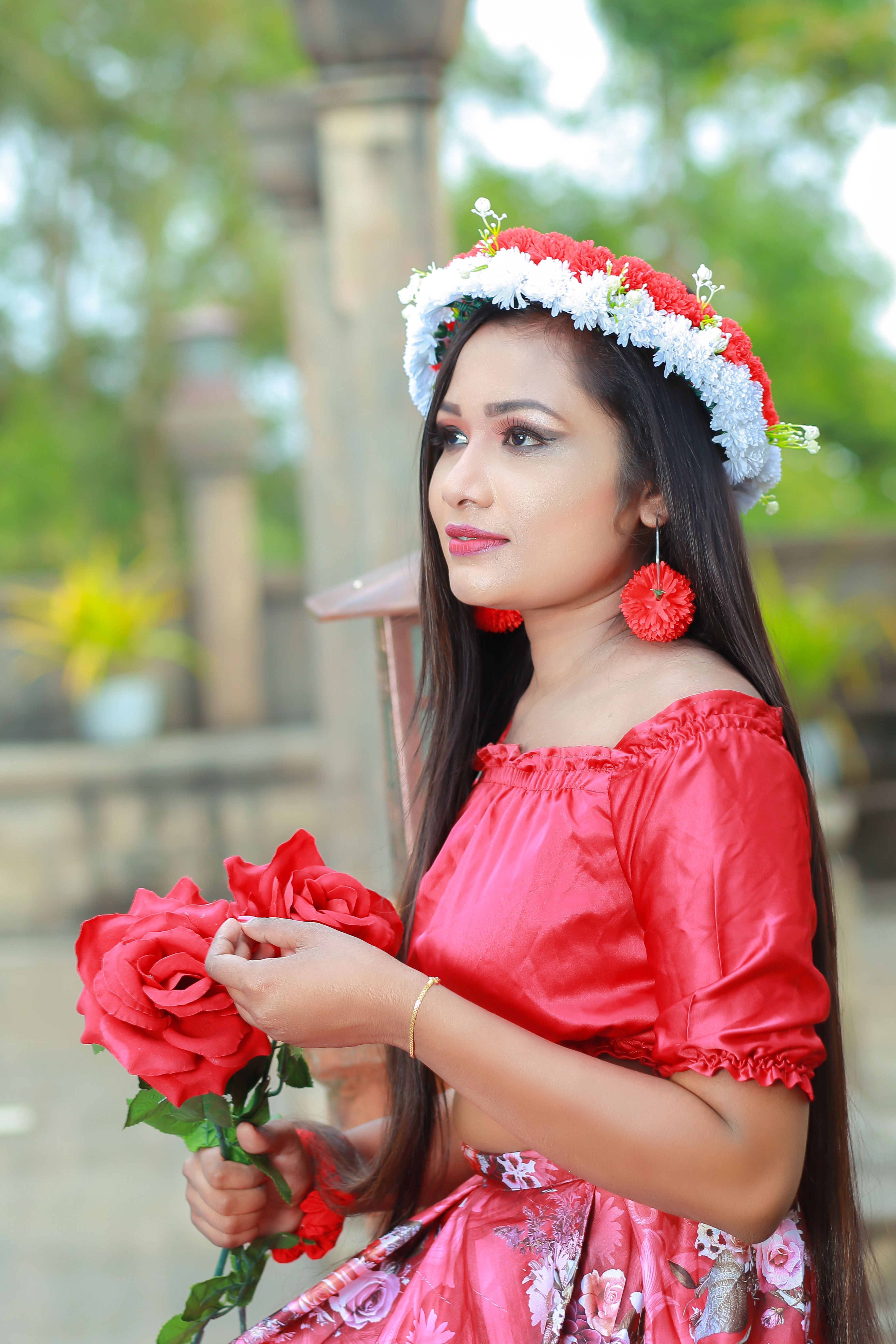 Elegant woman in a red floral dress holding roses outdoors, exuding beauty and grace.