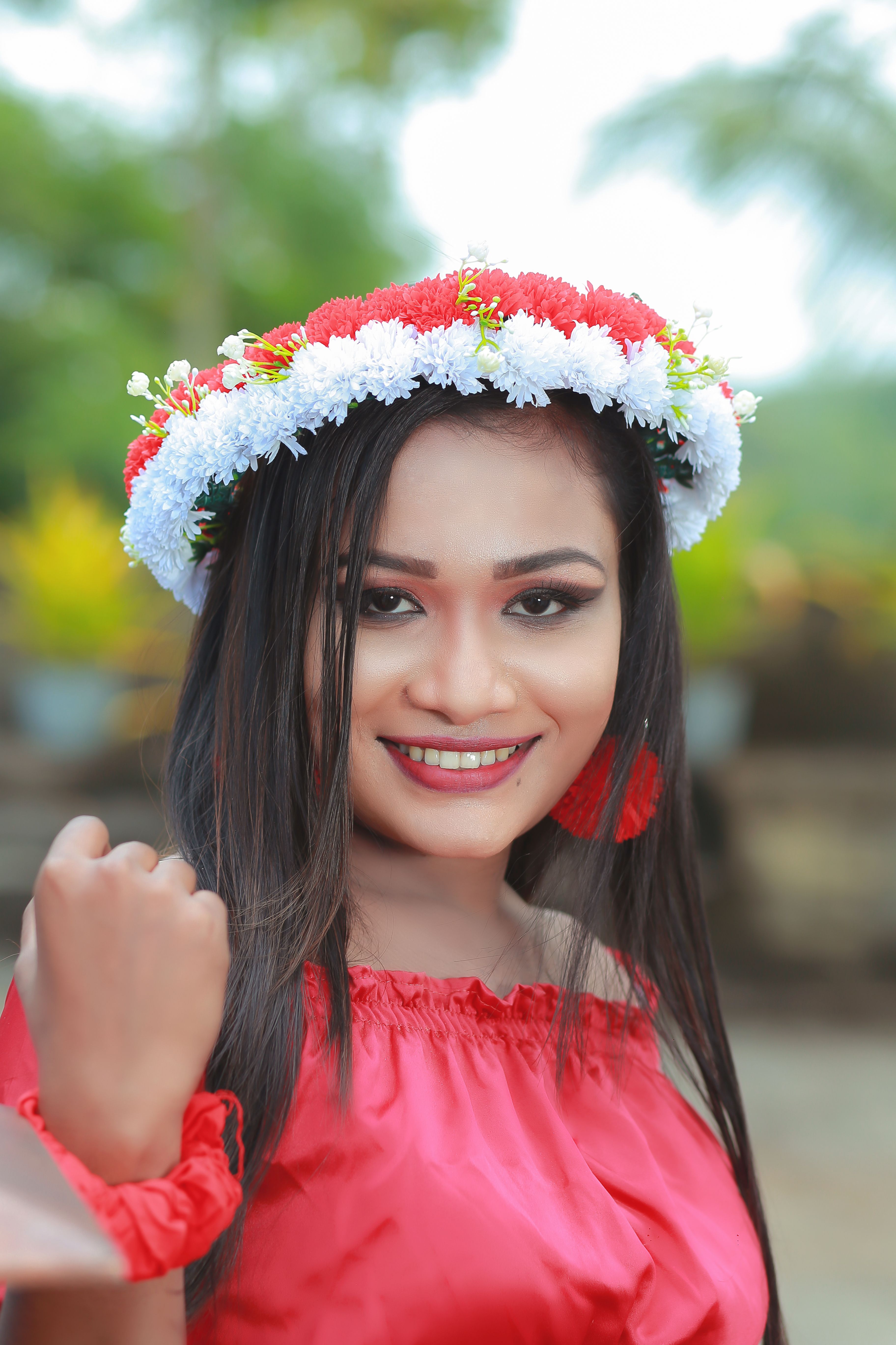 Portrait of a smiling woman outdoors wearing a vibrant floral headband and red attire.