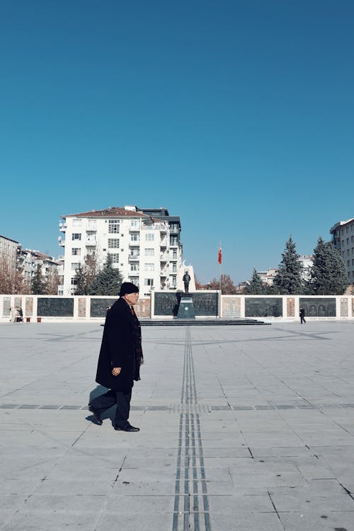 Man in Coat Walking on Sunlit Square